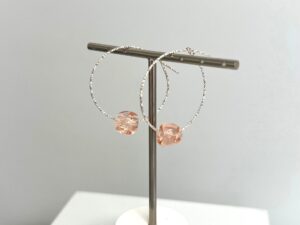 Femme portant des boucles d'oreilles créoles en argent avec perle rose artisanale.