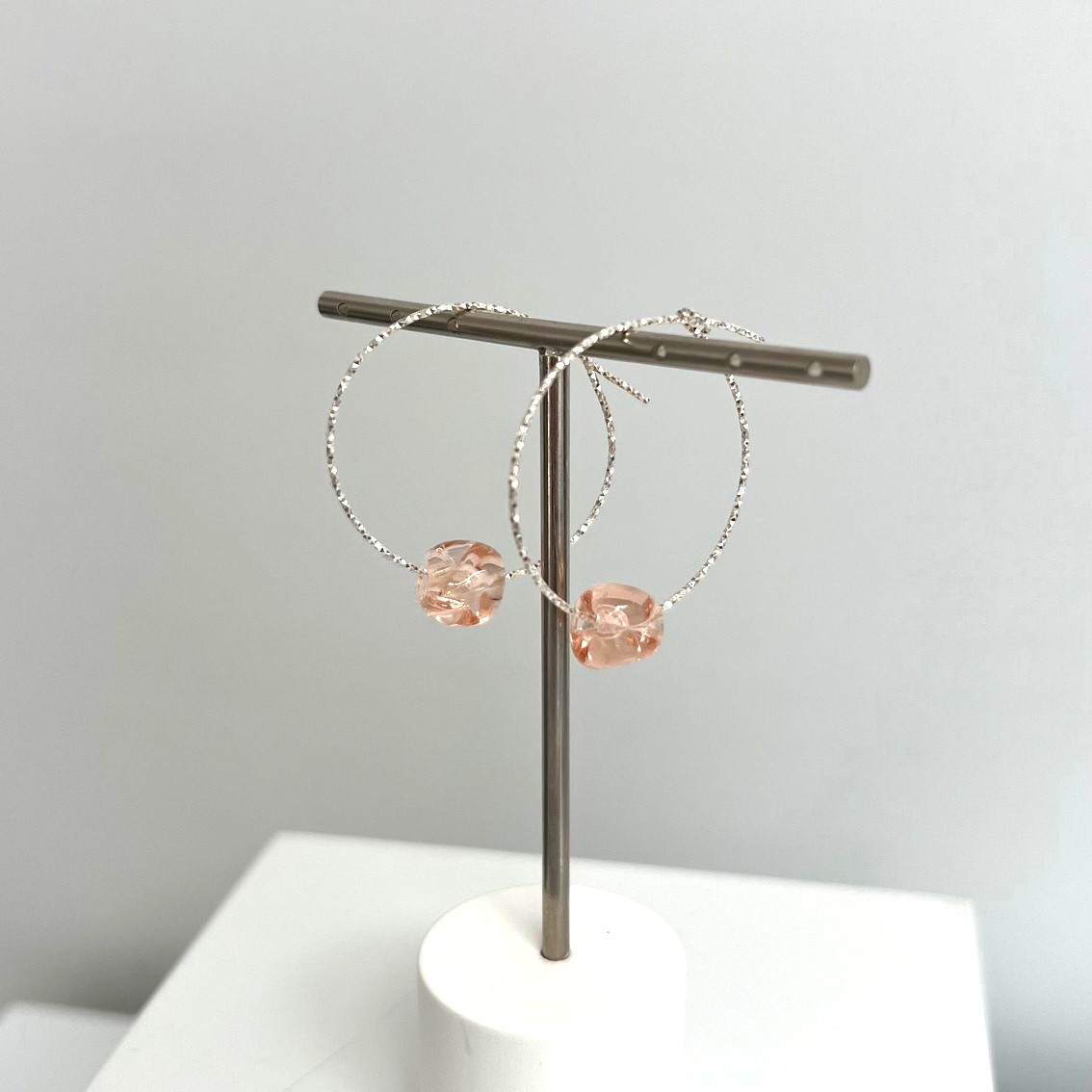 Femme portant des boucles d'oreilles créoles en argent avec perle rose artisanale.
